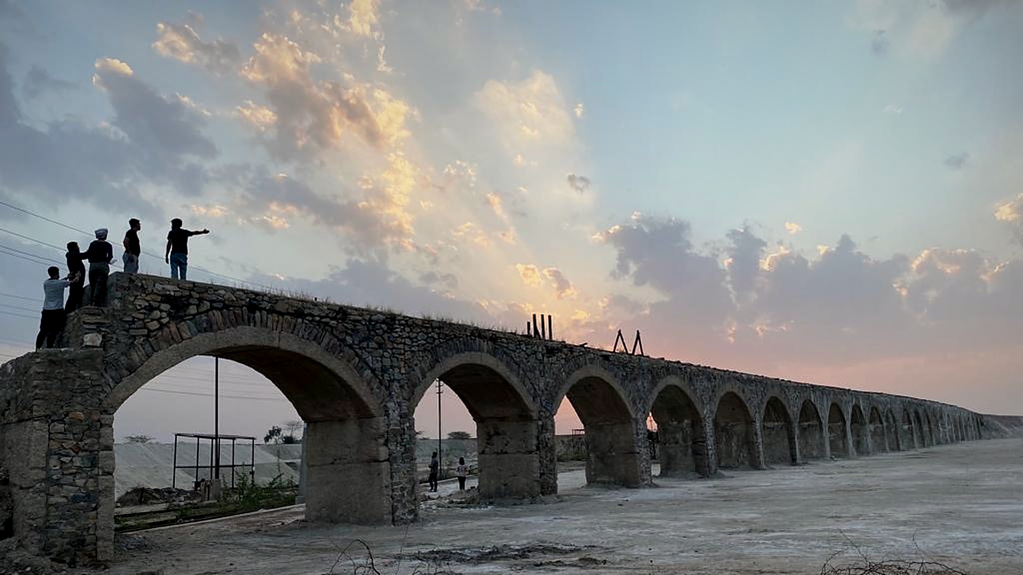 Crew on a stone-arched aqueduct at sunset
